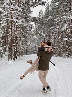 a man carrying a woman on his back while walking through the snow in front of trees