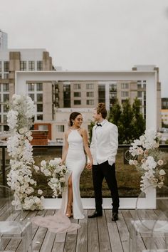 a bride and groom standing on a wooden deck with white flowers in front of them