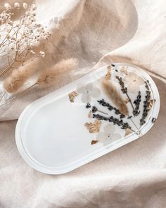 a white plate with dried flowers on it next to some dry grass and other plants