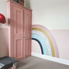 a room with a pink cabinet and rainbow wall mural