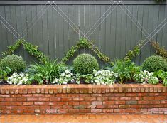 a brick planter filled with lots of plants next to a wooden fence and wall