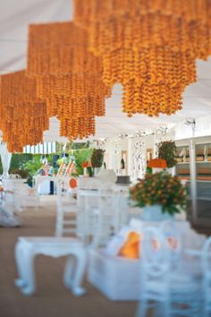 an outdoor event with white chairs and orange chandeliers hanging from the ceiling above them