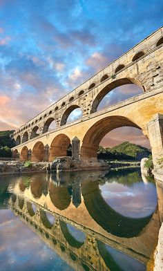 an old stone bridge spanning the width of a river under a cloudy blue and pink sky