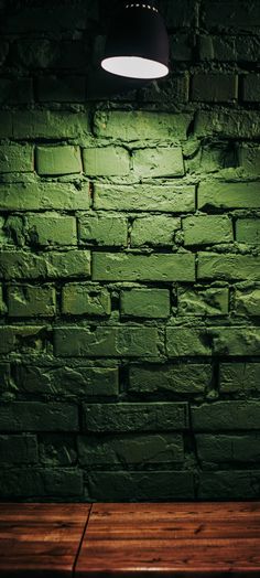 a dark green brick wall with a light on the side and wooden floor below it