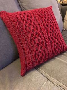 a red knitted pillow sitting on top of a couch next to a gray sofa