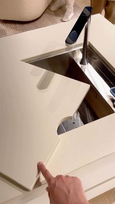 a person pointing at an open sink in a kitchen with white countertops and cabinets