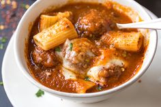 a white bowl filled with pasta and meatballs in tomato sauce on top of a plate