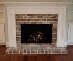 a fire place in the middle of a living room with wood floors and white walls