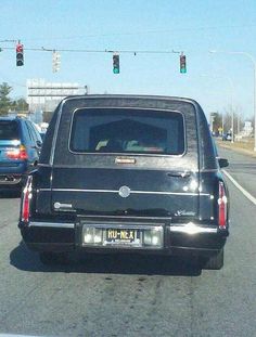 the back end of a black car driving down a street with traffic lights above it