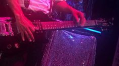 a man playing an electric bass guitar in a dark room with purple lights on it