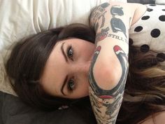 a woman laying on top of a bed with tattoos on her arm and leg, next to a polka dot pillow