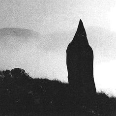 a black and white photo of a person standing on top of a hill in the fog