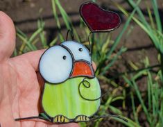 a hand holding a stained glass bird with a red heart on it's back