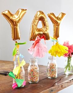 some gold balloons are in vases with flowers and confetti on the table