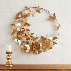 a metal wreath with gold butterflies hanging on the wall next to a white candle and wooden dresser