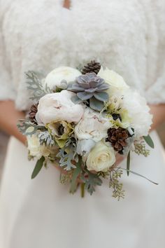 a bridal bouquet with succulents and pine cones is displayed on the bride's dress