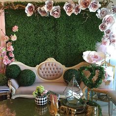 a couch and table with flowers on it in front of a green wall that is decorated with pink roses