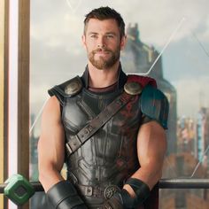 a man dressed as thor stands in front of a window with his hands on his hips