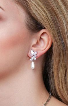 a woman wearing a pair of earrings with pearls on the end of each earpiece