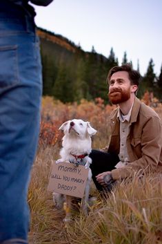 a man sitting in the grass with his dog holding a sign that says mommy will you marry daddy?