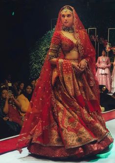 a woman in a red and gold bridal gown on the runway at a fashion show