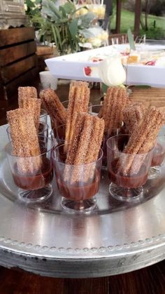 small glass cups filled with churro sticks on a silver tray in front of flowers