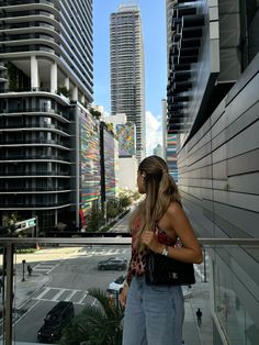 a woman standing on a balcony looking out at the cityscape with tall buildings in the background