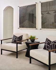 two white chairs sitting next to each other in front of paintings on the wall above them