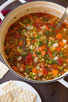 a pot filled with soup and vegetables next to crackers