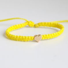 This bracelet is made of yellow waterproof rope and a gold plated heart charm. Cheap Yellow Friendship Bracelets, Gold Heart Jewelry With Adjustable Cord, Yellow Adjustable Cord Bracelet, Handmade Gold Nylon Cord Friendship Bracelets, Handmade Gold Friendship Bracelets With Nylon Cord, Trendy Gold Braided Bracelet With Sliding Knot, Gold Heart Friendship Bracelets With Sliding Knot, Handmade Gold Braided Bracelet With Nylon Cord, Handmade Gold Braided Bracelet