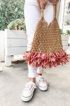 a woman is holding a bag made out of crocheted yarn and pink flowers