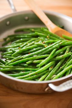 green beans are being cooked in a skillet with wooden spoons on the side