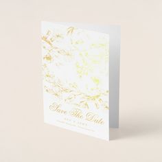 a white card with gold foil on it that says, save the date and flowers