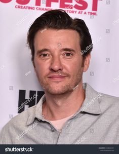 a man in grey shirt posing for the camera with his eyes closed and one eye open