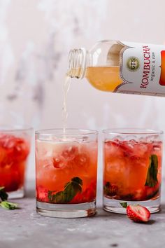 a bottle of booze being poured into glasses filled with ice and strawberries