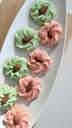 four desserts are arranged on a white platter with almonds and green frosting