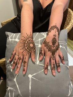 two hands with henna tattoos on them sitting next to a gray pillow and chair