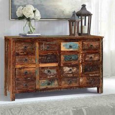 an old wooden dresser with drawers and vases on it's top, in front of a white wall