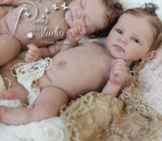 two baby dolls laying next to each other on a white blanket with gold trimmings