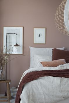 a bedroom with pink walls and white linens on the bed, along with two framed pictures