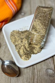 a small white plate topped with spices and a spoon next to it on top of a wooden table