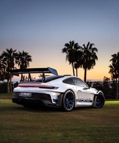 a white sports car parked on top of a lush green field next to palm trees