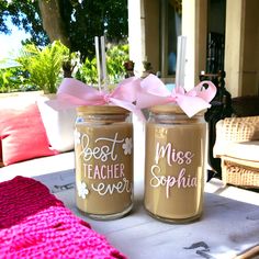 two mason jars with pink bows are sitting on a table outside, one has the words best teacher ever written on it