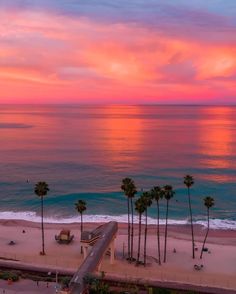 an aerial view of a beach with palm trees and the ocean in the background at sunset