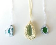 three pieces of crochet are hanging on a white surface, one is green and the other is blue