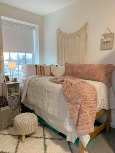 a bedroom with a white bed and pink comforter on top of it, next to a window