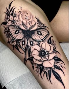 a woman's thigh with black and white tattoos on her legs, the butterfly is surrounded by flowers