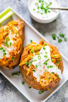 two baked potatoes on a white plate with sour cream and green onion garnish