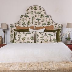 a bed with white linens and palm trees on the headboard, along with two lamps