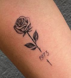 a small rose tattoo on the right thigh, with an arrow and date tattooed in black ink